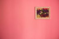 a pink wall with a single framed painting of flowers hung in the top right corner