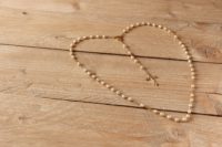 rosary beads laying on a wood floor, in the shape of a heart