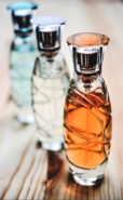 Three bottles of perfume, the one in front is amber, the one in the middle is clear, and the one in the back is turquoise