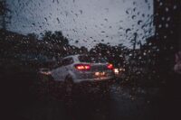 a view through a rain speckled window or windshield of a white car with its brake lights lit