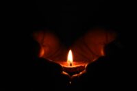 close up of two hands holding a tealight candle in the dark