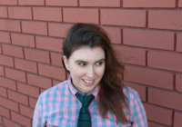 headshot of LJ Pemberton, a white woman with long brown hair smiling and wearing a checked shirt and silk tie