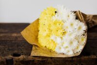 Yellow and white cut flowers, wrapped in brown paper, and laying on a wood table