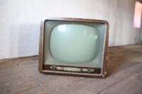 an antique television sitting on an unfinished wood floor with a white wall behind it