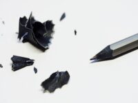 a black pencil with black pencil shavings scattered to its left, on a white background
