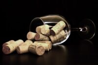 a wine glass full of bottle corks, tipped over on its side, against a black background