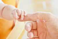 a baby grasps the index finger of an adult