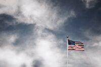 an American flag flying in the breeze alone, against a gray cloudy sky