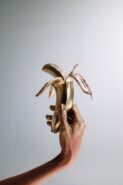 a hand holding a half-peeled banana. both the fruit and the hand appear to be turning into gold.