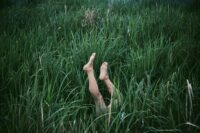 a pair of naked legs and feet stick out from long grasses