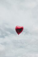 a red heart balloon floating in a cloudy gray sky